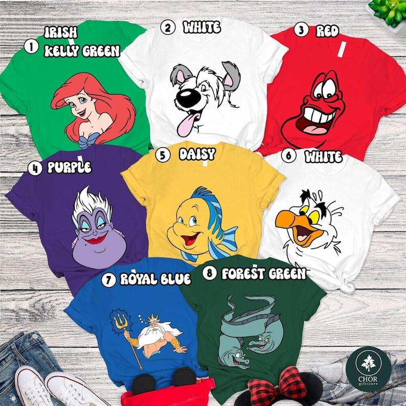 A collection of cartoon character t-shirts, each with a different color and design, laid out on a wooden surface.