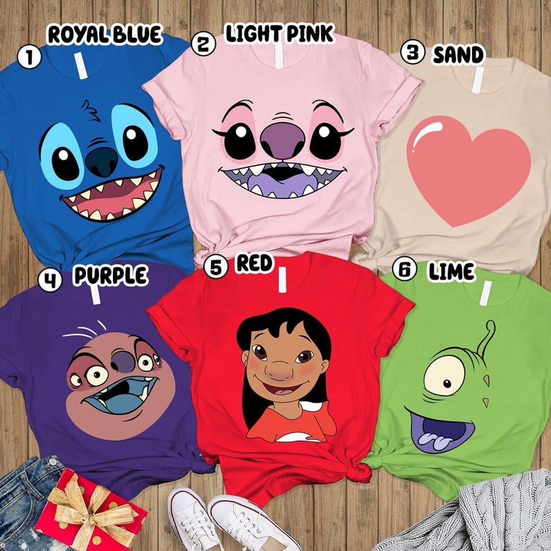 May include: A collection of six colorful t-shirts featuring cartoon character faces. The shirts are in royal blue, light pink, sand, purple, red, and lime green. Each shirt has a different character design, including a heart graphic.