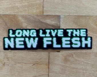 Peut inclure: Un autocollant noir et blanc avec du texte vert qui dit "Long Live The New Flesh".