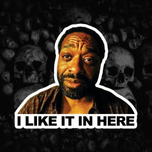 May include: A sticker featuring a person with a beard and a plaid shirt against a dark background of skulls. The person has a tear on their cheek and a somber expression. Below the person, the text I LIKE IT IN HERE is printed in white.