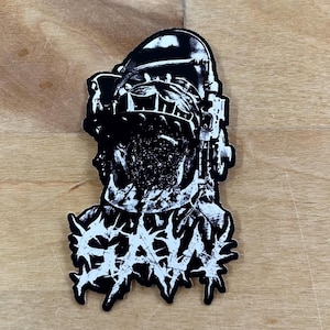 May include: Black and white sticker with a graphic of a person wearing a helmet with a barbed wire design and the word "SAW" in a stylized font.