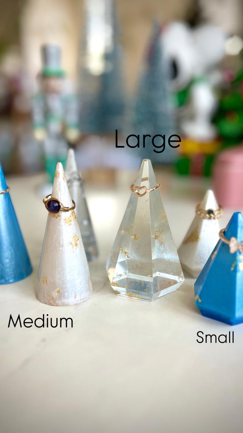May include: Three ring display stands in different sizes: small, medium, and large. The small stand is blue, the medium stand is white with gold flecks, and the large stand is clear with gold flecks. Each stand has a ring on it.