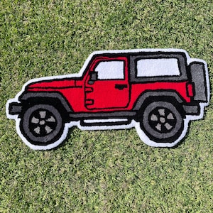 May include: A tufted rug shaped like a red off-road vehicle with a black roof, dark gray wheels, and a spare tire on the back. The design features bold black outlines and a white border, showcasing a side profile of the vehicle with a boxy frame.