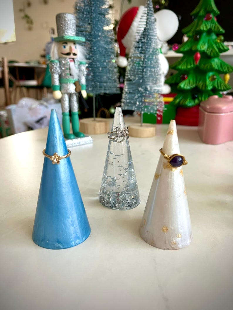 May include: Three ring holders, one blue, one clear with glitter, and one white with gold flecks. Each holder has a ring on it.