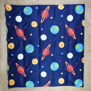 May include: A blue weighted blanket with a space theme. The blanket features a repeating pattern of planets, stars, and moons.
