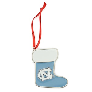 May include: A light blue stocking-shaped ornament with a white cuff and a silver outline. The ornament features the University of North Carolina logo and a red ribbon for hanging. A festive holiday decoration.