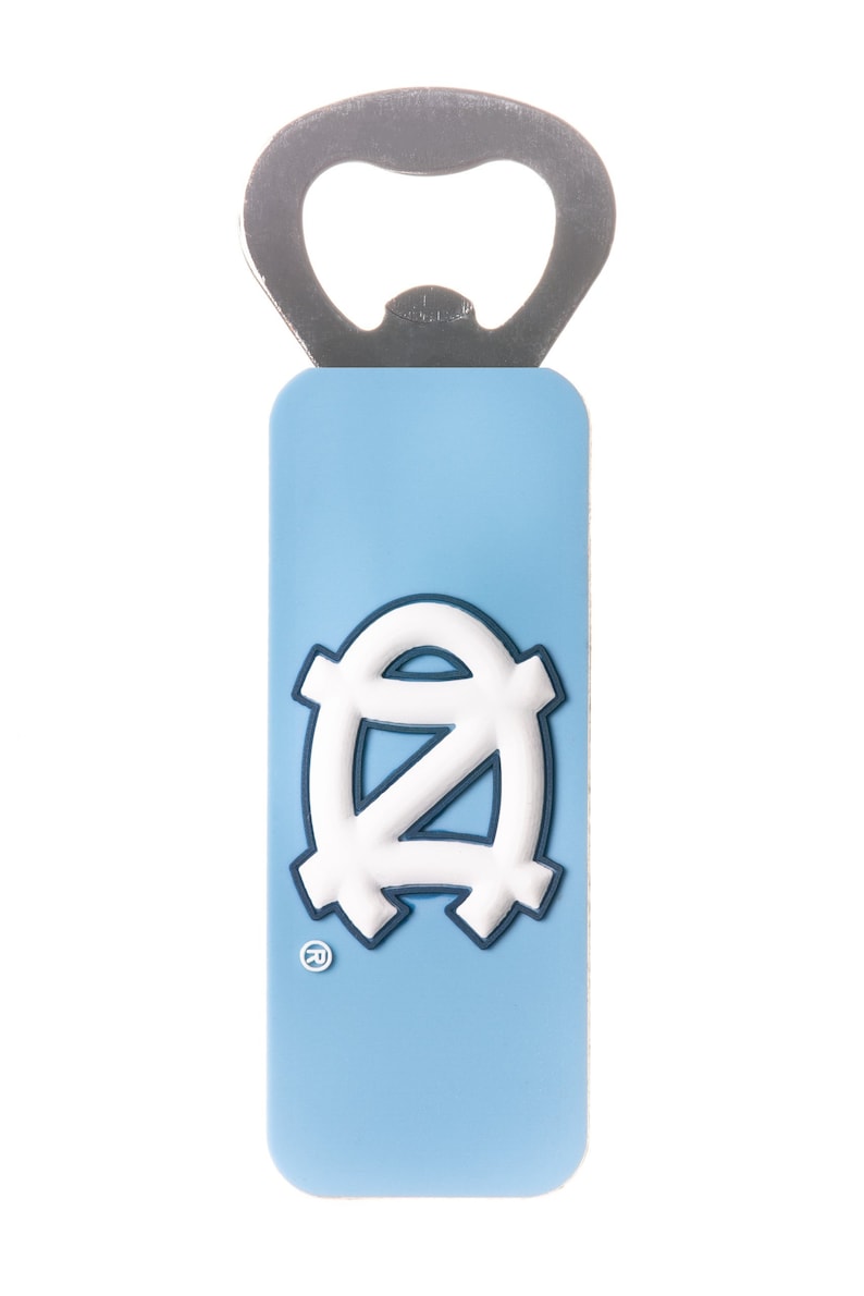 Op de afbeelding: Een blauwe en witte flesopener met het logo van de University of North Carolina Tar Heels. De opener heeft een zilveren flesopener bovenop.