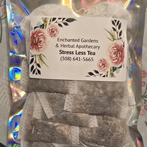 May include: A clear, iridescent bag containing tea bags. A white label with the text "Enchanted Gardens & Herbal Apothecary Stress Less Tea" is affixed to the bag. The label features floral and botanical illustrations, including pink roses and green leaves.