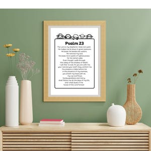 Op de afbeelding: Zwart-witte printbare wandkunst met Psalm 23, een bijbelvers over God als herder. De tekst wordt omringd door een decoratieve rand van schapen.