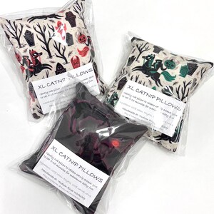May include: Three XL catnip pillows in clear packaging. The pillows have Halloween-themed patterns with images of tombstones, trees, and a headless horseman. The text "XL CATNIP PILLOWS" is printed on each pillow.