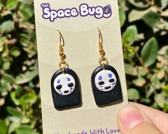 May include: A pair of gold dangle earrings with black and white No Face character from the movie Spirited Away. The earrings are handmade and have the text "The Space Bug" on the card.