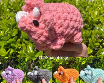 May include: A set of five crocheted dinosaur plushies in different colors: purple, gray, orange, blue, and pink. The dinosaurs are all the same size and have a similar design, with a long snout, three horns, and a small tail.