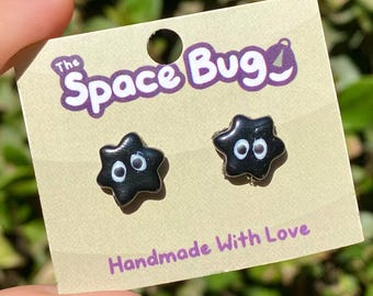 May include: A pair of black star-shaped earrings with white eyes. The earrings are on a card that says "The Space Bug" and "Handmade with Love".