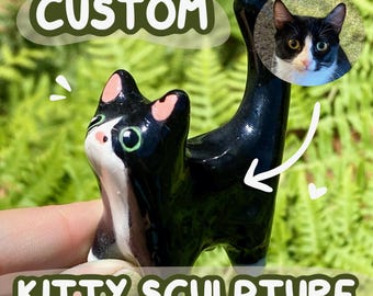 May include: A black and white ceramic cat sculpture with pink ear accents and green eyes. The sculpture is held in a hand and has the text "CUSTOM" and "KITTY SCULPTURE" in a green bubble. A photo of a cat is also included.
