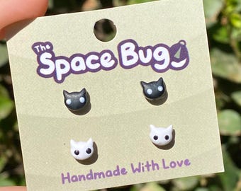 May include: A card with the text "The Space Bug" and the words "Handmade With Love" on it. There are four small black and white cat face earrings on the card.