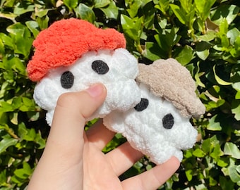 May include: Two plush white mushroom-shaped hair scrunchies with black eyes. One scrunchie has a coral-colored top and the other has a light brown top.