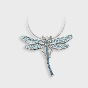 Puede incluir: Un collar con colgante de libélula plateada. La libélula tiene alas de esmalte azul claro con un patrón detallado, un cuerpo de piedra preciosa azul y una cola a juego. La cadena del collar es un cable fino y plateado.