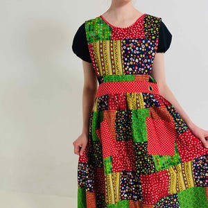 May include: A patchwork dress with a vibrant mix of red, green, yellow, and navy blue patterned squares. The dress has a red polka dot waistband and a black top. The dress is a vintage style.