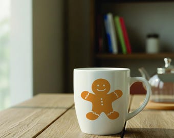 May include: A white ceramic mug featuring a centered graphic of a golden-brown gingerbread person. The gingerbread figure has a smiling face, three small white dots on its torso, and white wavy lines on its arms and legs. The mug has a handle.