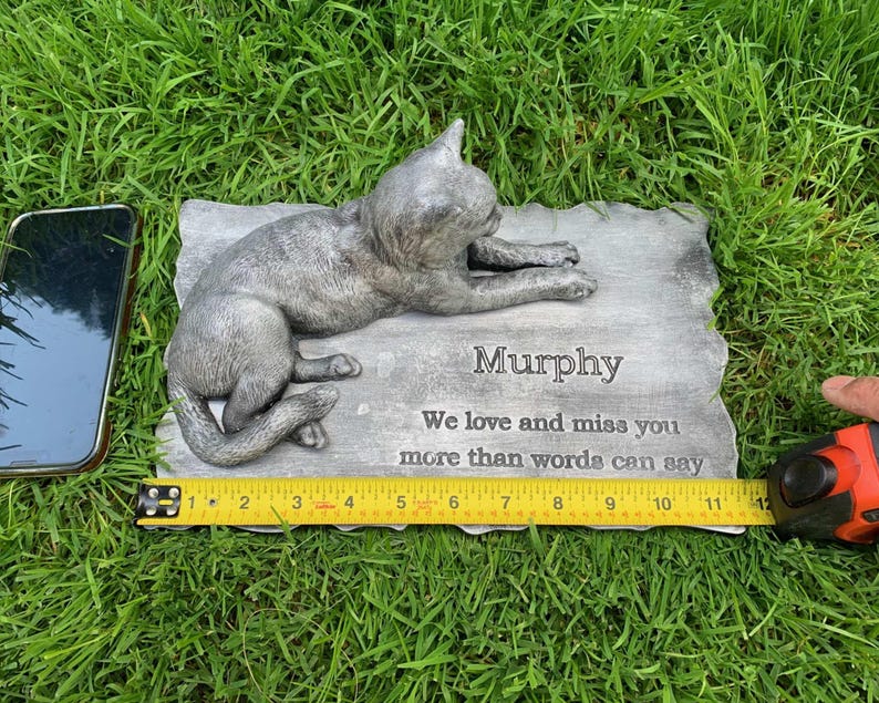 K&ouml;nnte beinhalten: Eine graue Gedenktafel aus Beton mit einer geformten Katzenfigur. Die Tafel tr&auml;gt die Aufschrift "Murphy We love and miss you more than words can say".