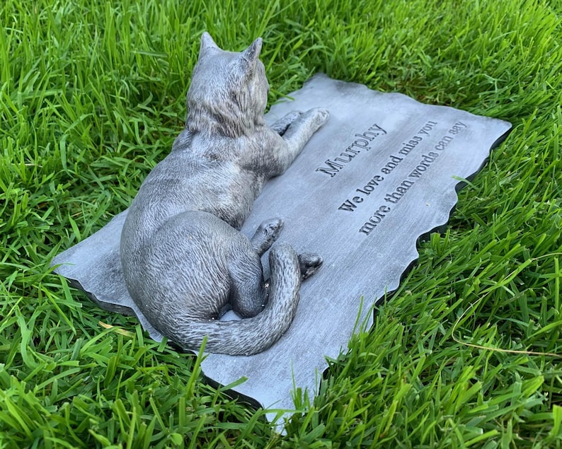 K&ouml;nnte beinhalten: Ein graues Beton-Katzen-Denkmal mit der Inschrift "Murphy. We love and miss you more than words can say."