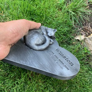 May include: A gray heart-shaped memorial plaque with a sleeping cat sculpture. The plaque reads "Winston I love and miss you more than words".