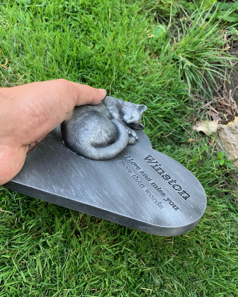 May include: A gray heart-shaped memorial plaque with a sleeping cat sculpture. The plaque reads "Winston I love and miss you more than words".
