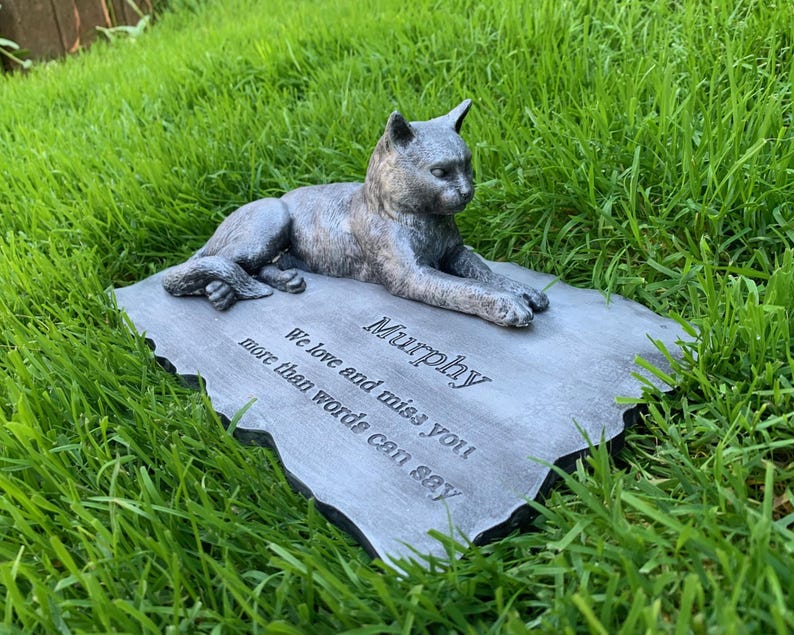 K&ouml;nnte beinhalten: Ein grauer Steindenkmal mit einer darauf liegenden, geformten Katze. Der Stein tr&auml;gt die Worte "Murphy" und "We love and miss you more than words can say" eingraviert.