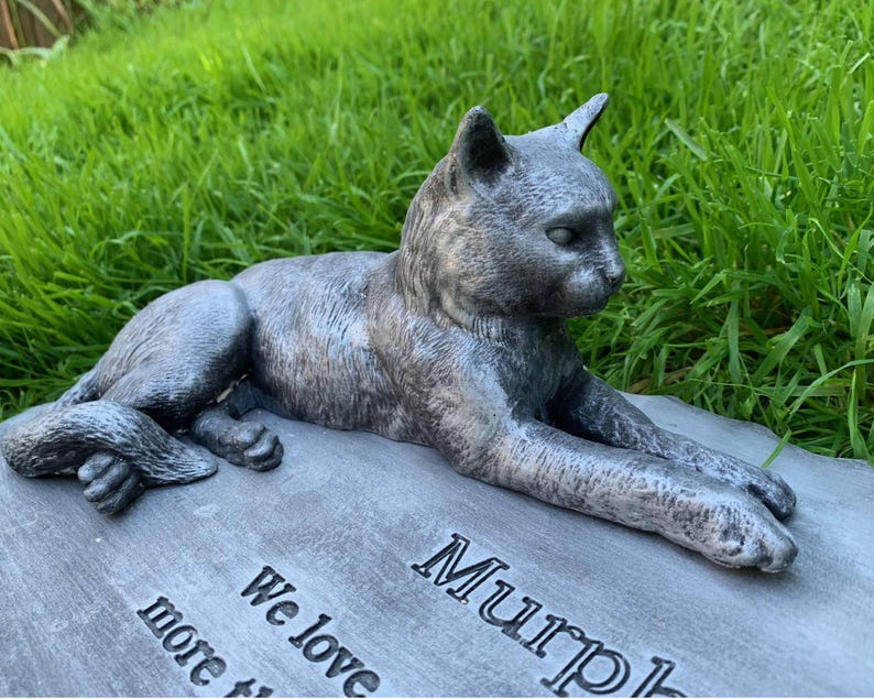 K&ouml;nnte beinhalten: Ein graues Beton-Katzen-Denkmal mit dem Namen "Murphy" eingraviert. Die Inschrift lautet auch "We love you more than words can say".