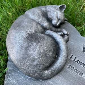 May include: A gray stone memorial with a sculpted sleeping cat. The inscription reads "We love and miss you more than words can say."