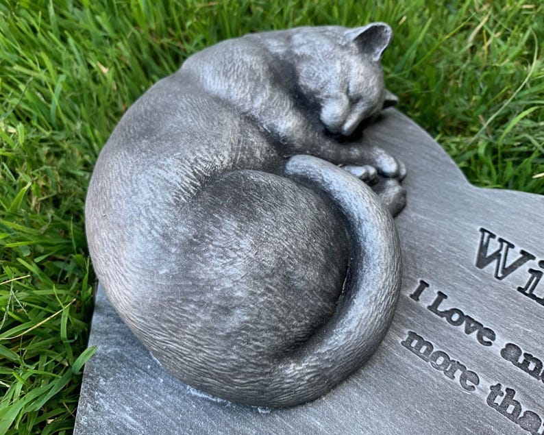 May include: A gray stone memorial with a sculpted sleeping cat. The inscription reads "We love and miss you more than words can say."