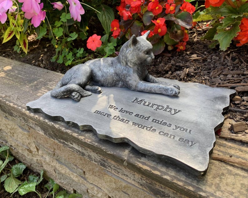 K&ouml;nnte beinhalten: Ein grauer Steindenkmal mit einer darauf liegenden, geformten Katzenfigur. Der Stein tr&auml;gt die Inschrift "Murphy We love and miss you more than words can say."
