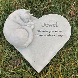 May include: A gray heart-shaped stone memorial with a sleeping cat sculpture. The stone has the inscription "Jewel We miss you more than words can say."