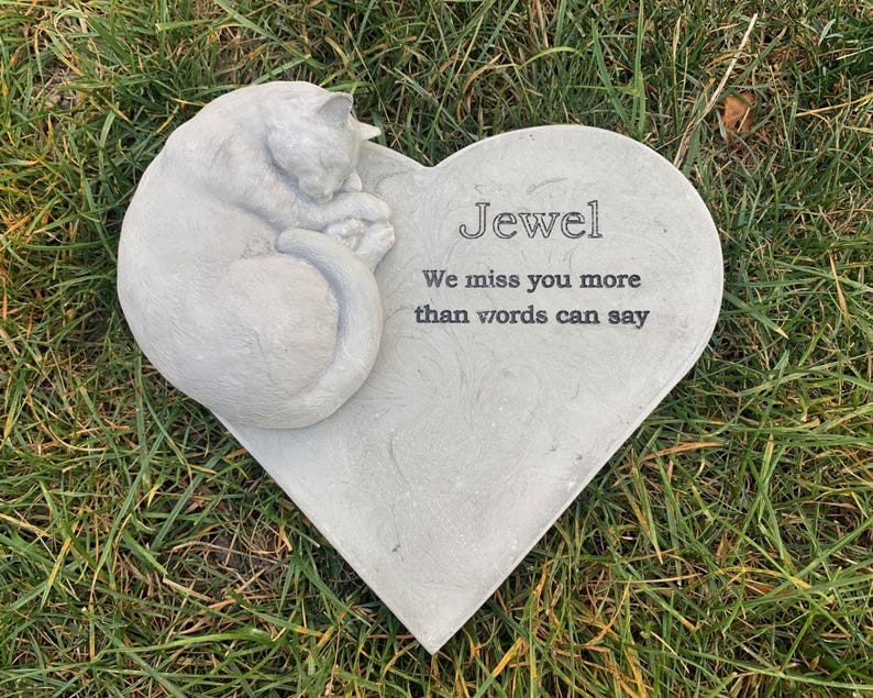 May include: A gray heart-shaped stone memorial with a sleeping cat sculpture. The stone has the inscription "Jewel We miss you more than words can say."