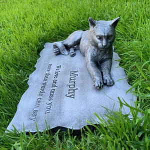 K&ouml;nnte beinhalten: Ein grauer Gedenkstein aus Beton mit einer darauf liegenden, geformten Katze. Der Stein tr&auml;gt die Inschrift "Murphy" und den Text "We love and miss you more than words can say."