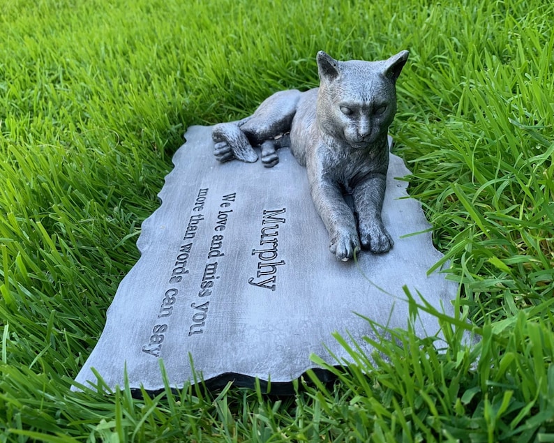 K&ouml;nnte beinhalten: Ein grauer Gedenkstein aus Beton mit einer darauf liegenden, geformten Katze. Der Stein tr&auml;gt die Inschrift "Murphy" und den Text "We love and miss you more than words can say."