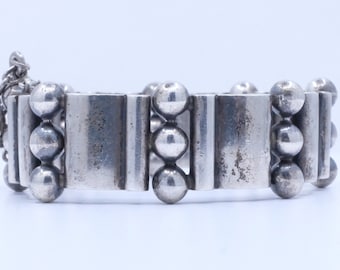 May include: A silver bracelet with a series of rectangular links and spherical beads. A small chain hangs from one end. The bracelet has a vintage, worn appearance. The bracelet is made of silver.