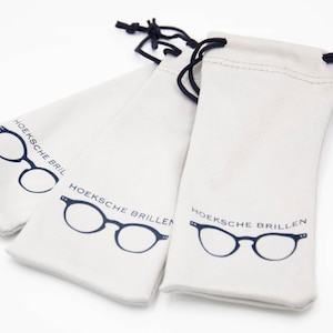 May include: Three off-white drawstring pouches with a dark blue eyeglasses graphic and the text "HOEKSCHE BRILLEN". The pouches are made of a soft fabric and have black drawstrings.