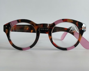 Könnte beinhalten: Runde Lesebrille aus Schildpatt mit rosa Akzenten und einer +2,00-Vergrößerung. Die Brille hat einen schwarzen Rahmen mit einem braunen und roten Schildpattmuster.