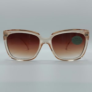 May include: A pair of light brown, oversized sunglasses with brown gradient lenses. The sunglasses have a 100% UV protection label attached to the right lens.