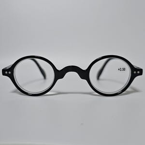 May include: Black, round-frame spectacles with clear lenses. The glasses feature a keyhole bridge and small rivets on the temples. The right lens is marked with "+3.50".
