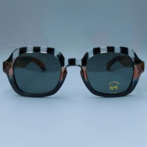 Może przedstawiać: Czarno-białe kwadratowe okulary przeciwsłoneczne z polaryzacyjnymi szkłami. Okulary mają złotą etykietę z napisem "POLARIZED" i "key" z "UV 400" poniżej.