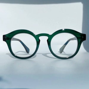 Puede incluir: Gafas redondas de montura verde con lentes transparentes. La montura es de plástico y tiene un brillo sutil.