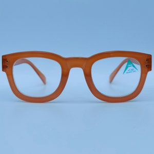 May include: Orange plastic framed eyeglasses with clear lenses. The right lens has a sticker that reads " +1.50 Aspheric Lens".