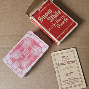 Puede incluir: Un juego de cartas vintage de Blancanieves y los siete enanitos de la serie Pepys. Incluye una caja de cartón roja, una baraja con el reverso de patrón de ladrillos rosa con una ilustración central y un pequeño folleto titulado Rules for the Game of Snow White.