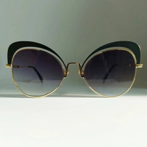Könnte beinhalten: Schwarze Cat-Eye-Sonnenbrille mit goldenem Metallrahmen und dunkelgrauen Gläsern.