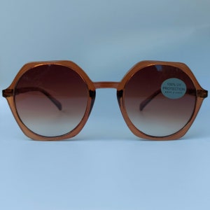 Op de afbeelding: Bruine, achtkantige zonnebril met een verlooplens. De zonnebril heeft een sticker op de rechterlens met de tekst "100% UV PROTECTION HAVE A LOOK".
