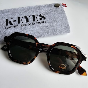 Op de afbeelding: Zonnebril met schildpadpatroon en donkere glazen, met de tekst "TROPZ" en "POLARIZED UV400." De zonnebril wordt geleverd met een grijze vilten etui met de tekst "K-EYES LUNETTES - BAIE DE ST TROPEZ."