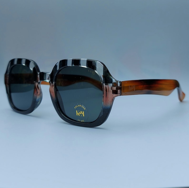 Może przedstawiać: Okulary przeciwsłoneczne w czarno-białe paski z brązowymi oprawkami typu "ż&oacute;łwiowy". Soczewki są ciemne i spolaryzowane. Okulary mają logo "key" i napis "polaryzowane" oraz "UV 400" na prawej soczewce.