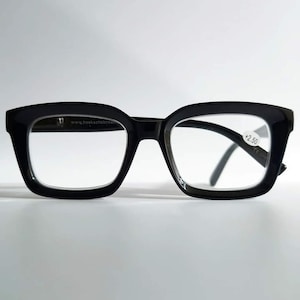 Peut inclure: Lunettes de lecture rectangulaires noires avec une puissance de +2,50. Le site web www.hoekchebrillen.nl est imprimé sur la branche gauche.